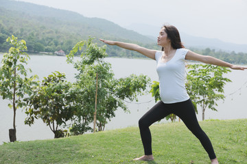 asian pregnant woman practicing yoga on green grass in public park.  concept of prenatal exercise, maternity, fitness, healthy lifestyle and relaxation.