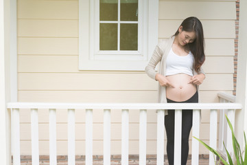 Young asian woman standing on balcony smiling with pleasure. Beautiful female expecting child having rest in front of her house