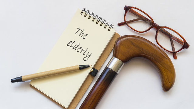 "The eldery" written on notebook that place on white background with staff, eyeglasses