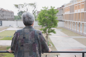 Senior elder standing on balcony looking at the city view, elderly asian woman enjoying nice weather on terrace