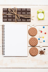Composition of sweets, green alarm clock and copybook