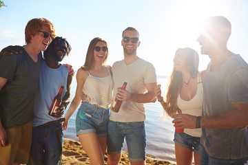 Laughing friends in sunglasses having rest by seaside