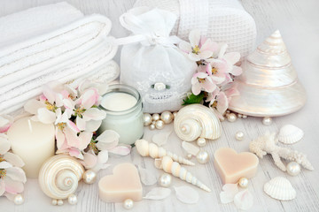 Natural spa beauty treatment cleansing products with apple blossom flowers, shells and pearls on distressed white wood background.