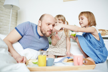 Little girls feeding father from spoon in bed