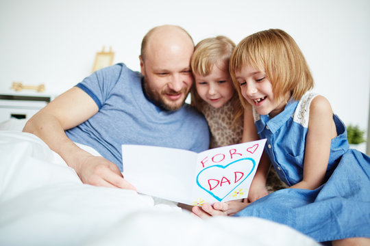 Little Sisters And Their Father Reading Greetings In Card