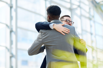Portrait of two business partners hugging  and smiling with happiness standing in modern glass hall...
