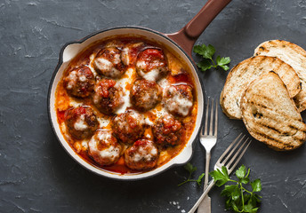 Baked meatballs with mozzarella and tomato sauce in a cast iron skillet on a dark background, top view - obrazy, fototapety, plakaty
