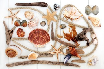 Abstract beach art with driftwood, rope, seashells, rocks and seaweed on white wood forming a...