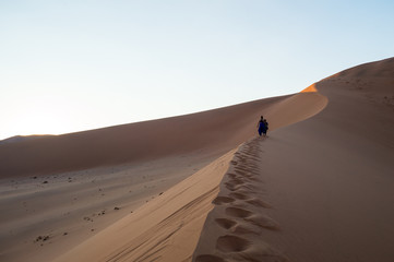 Fototapeta na wymiar Two Women Climbing Big Daddy Dune during Sunrise, Desert Landscape, Sossusvlei, Namibia