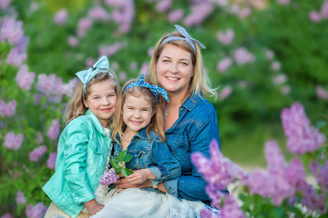 Mother woman with two cute smiling girls sisters lovely together on a lilac field bush all wearing stylish dresses and jeans coats.