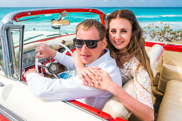 Beautiful couple bride in white lace wedding dress and groom sit in red retro car convertible...