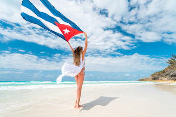 Beautiful young blond woman in white dress and bikini swimsuit is standing a back holding the cuban...