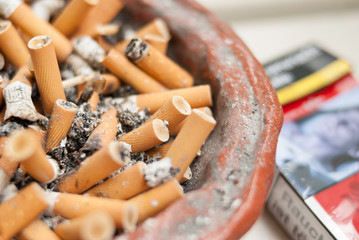 Cigarette butts in ashtray with cigarettes package