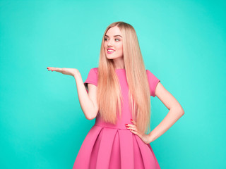 Smiling beautiful young woman in pink mini dress posing, presenting something