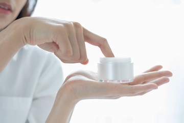 A beautiful woman asian using a skin care product, moisturizer or lotion taking care of her dry complexion. Moisturizing cream in female hands .