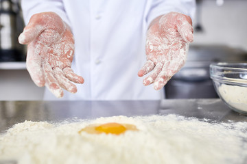 Fototapeta premium Hands of baker over workplace with pile of flour and raw yolk
