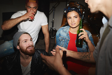 Group of modern young people drinking beer and chatting at party in underground night club
