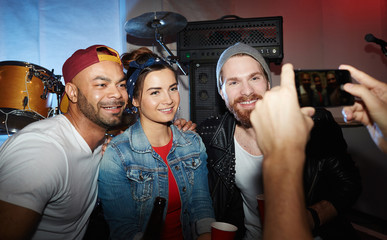 Group of modern trendy people chilling at night club party, posing for smartphone photo