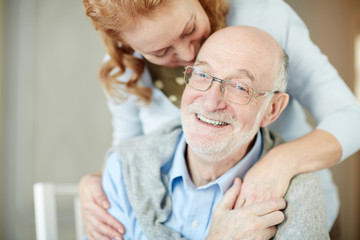 Obraz premium Smiley man with grey stubble looking at camera while his wife embracing him