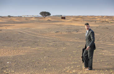 businessman in  a desert with a suitcase, looking at a map