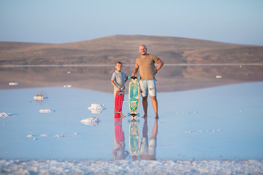 A boy with father walks along the shore of the lake on skate board. A Salt lake shore. A Salt Lake.