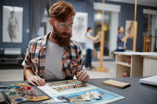 Portrait of contemporary bearded artist working in art studio painting oil pictures looking focused and concentrated