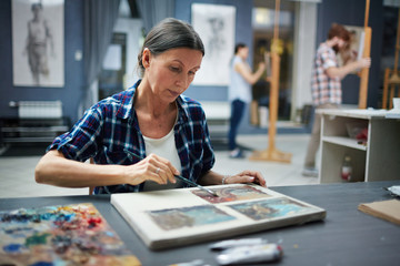Naklejka premium Portrait of mature student working in art studio painting pictures looking focused and concentrated
