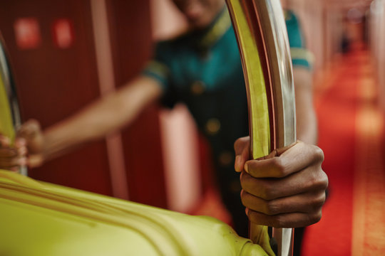Closeup portrait of African-American bellhop pushing luggage cart delivering bags to hotel rooms in hallway, helping guests