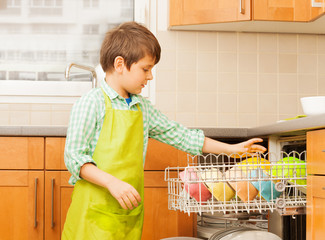 Kid boy getting out clean crockery of dishwasher