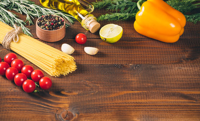 Spaghetti, tomatoes cherry, olive oil, herb and spices on old brown wooden background.