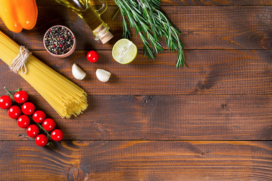 Spaghetti, tomatoes cherry, olive oil, herb and spices on old brown wooden background.