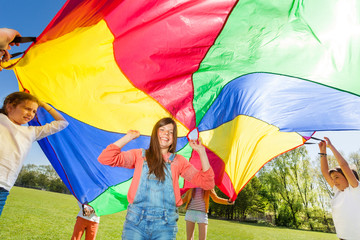 Happy friends playing rainbow parachute in summer