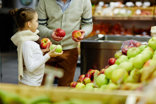 Portrait of little girl with dad choosing fresh ripe apples and other fruits in supermarket