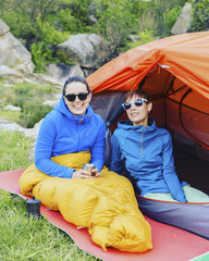 Camping on the river bank, two girls are sitting near the tent and talking.