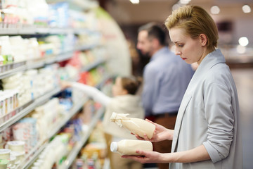 Side view portrait of blond woman choosing milk in dairy product department - obrazy, fototapety, plakaty