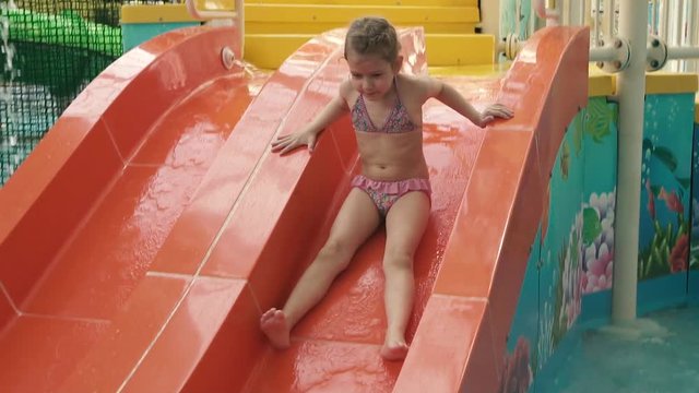 Little girl is riding a slide in a water park. slow motion