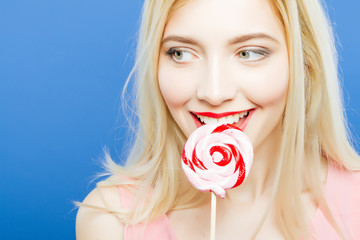 Amazing Playful Young Woman with Widely Opened Eyes and Charming Smile on Blue Background. Portrait of Funny Blonde with Lollipop in Hands in Studio.