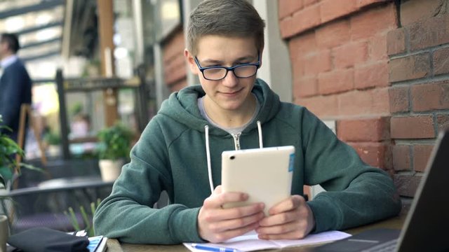 Happy, teenage boy browsing Internet on tablet in cafe in city
