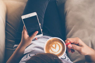 A young girl holding smartphone and drinking hot latte coffee in coffee shop