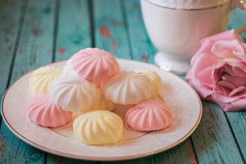 Delicate multi-colored marshmallows on white openwork plate. Still life with marshmallows, a Cup of tea and a pink rose on vintage background.