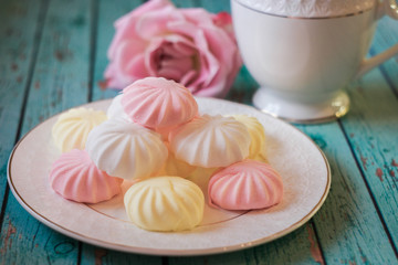 Delicate multi-colored marshmallows on white openwork plate. Still life with marshmallows, a Cup of tea and a pink rose on vintage background.
