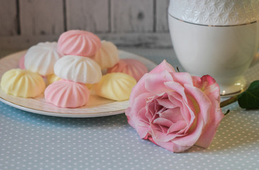 Delicate multi-colored marshmallows on white openwork plate. Still life with marshmallows, a Cup of tea and a pink rose on vintage background.