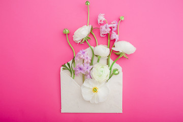 Fototapeta na wymiar Beautiful white and purple flowers, buds and paper envelope on pink background. Flat lay, top view. Flowers background.