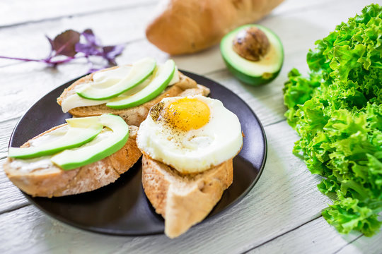 Tasty sandwiches with avocado and egg on a dark plate on wooden background