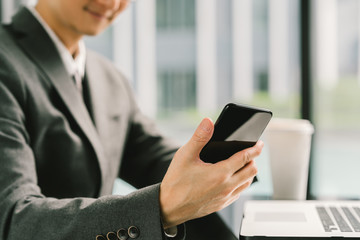 Asian businessman or entrepreneur using smartphoneand laptop, working in modern office. Business communication or technology gadget concept