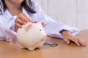 Obraz na płótnie Canvas Asian girl playing as a doctor balance money in Piggy Bank