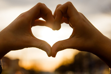 Obraz premium Hands in the shape of a heart glow at sunset