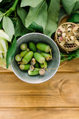 flower, gift and floral arrangement concept - top view on a bowl with green acorns, fresh rose on a wooden table, leaves and flower bud with drops of dew, design round jewelry box with flower petals
