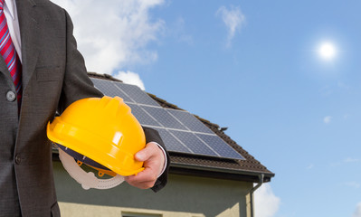 Ingenieur mit Helm vor einem Haus mit Solarzellen