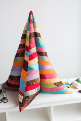 quilting - high pillow in the form of a pyramid of colorful quilted fabrics made of pieces of colored patchwork fabrics on the table next to the scissors, scraps of colored fabrics, coils of thread